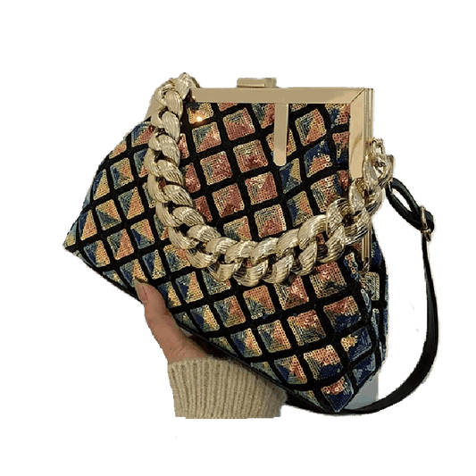 Multicolored patterned handbag with gold chain strap held by a hand on a white background